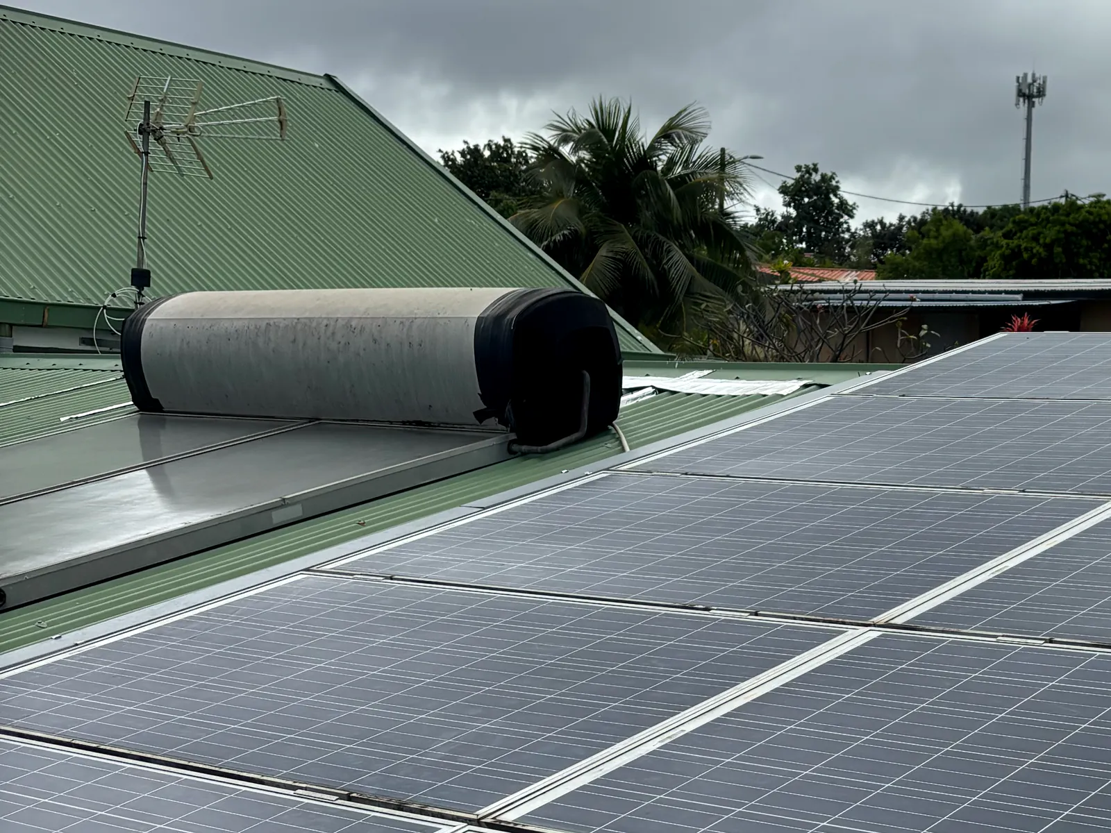 Ballon de chauffe-eau solaire installé sur une toiture en tôle, à côté de plusieurs rangées de panneaux photovoltaïques