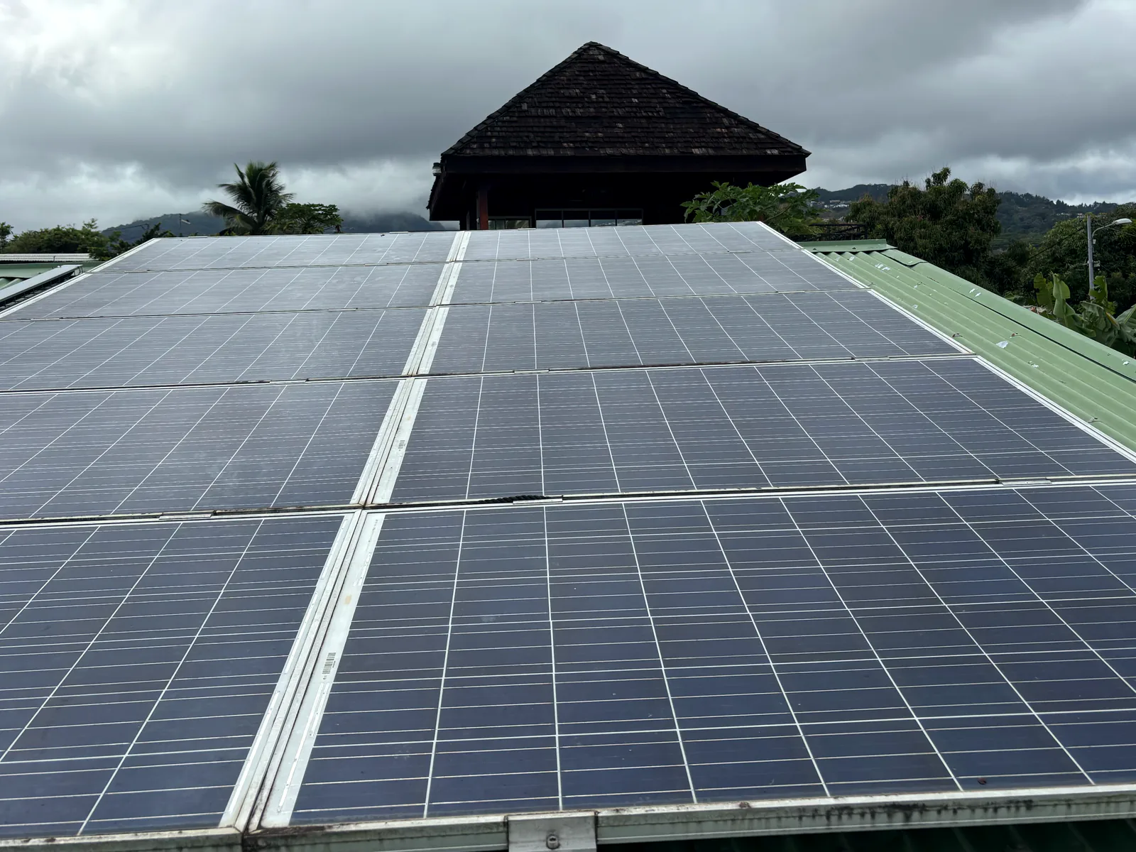 Panneaux solaires ternis par la poussière, dépôts noirs en bas du cadre, sur une toiture en tôle verte à Tahiti